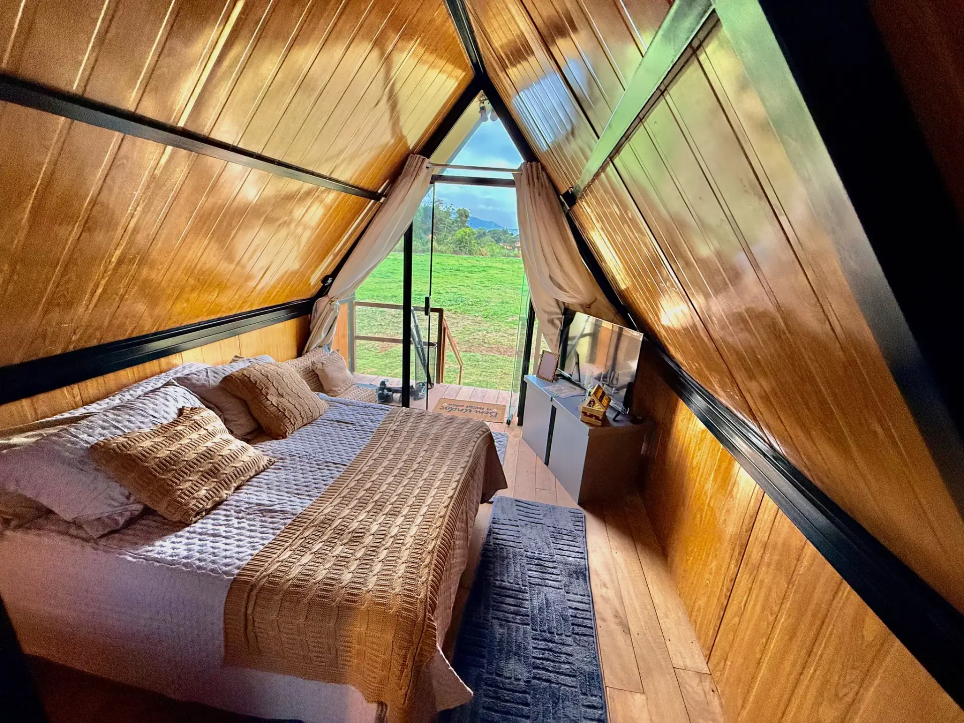 Quarto do chalé A-frame com janela de vidro para o campo