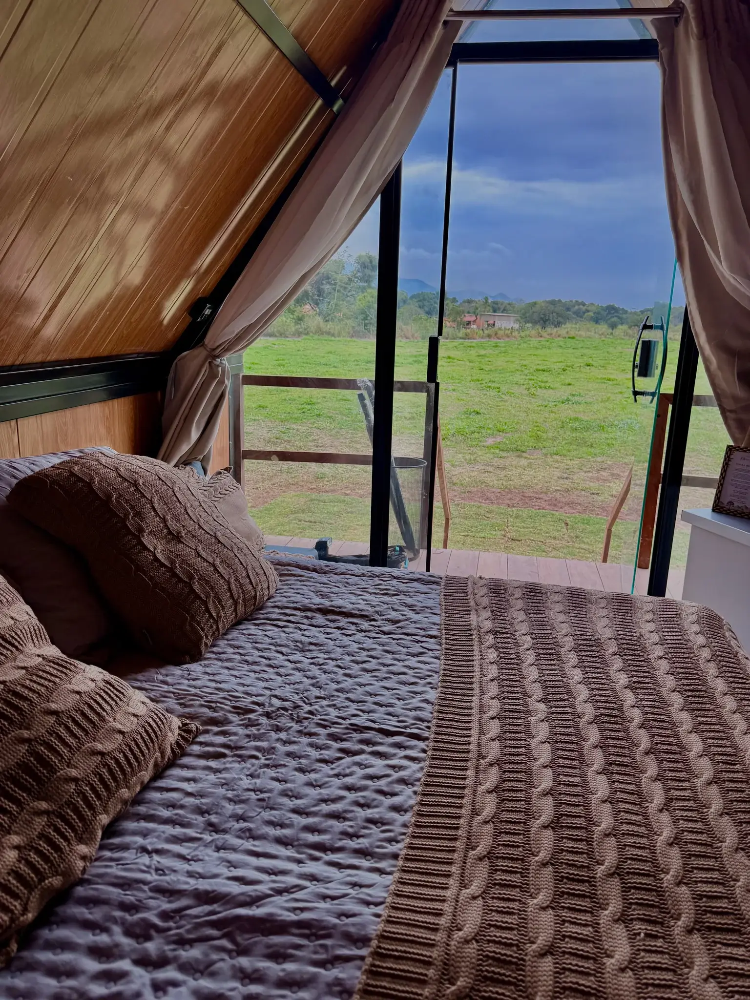 Cama de casal de frente para a porta de vidro aberta ao campo